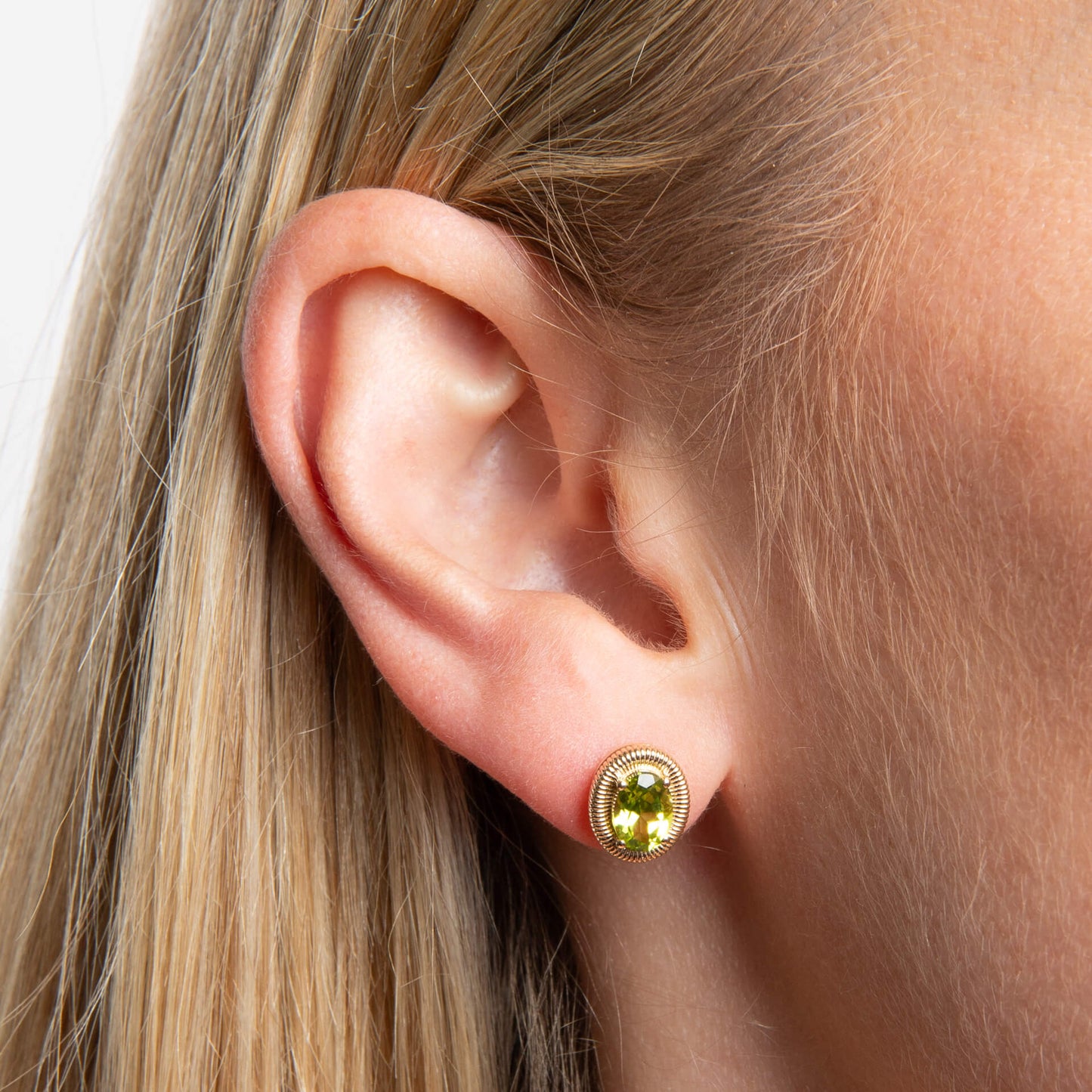 Model wearing 9ct yellow gold oval peridot stud earrings with sculpted ridged detailing