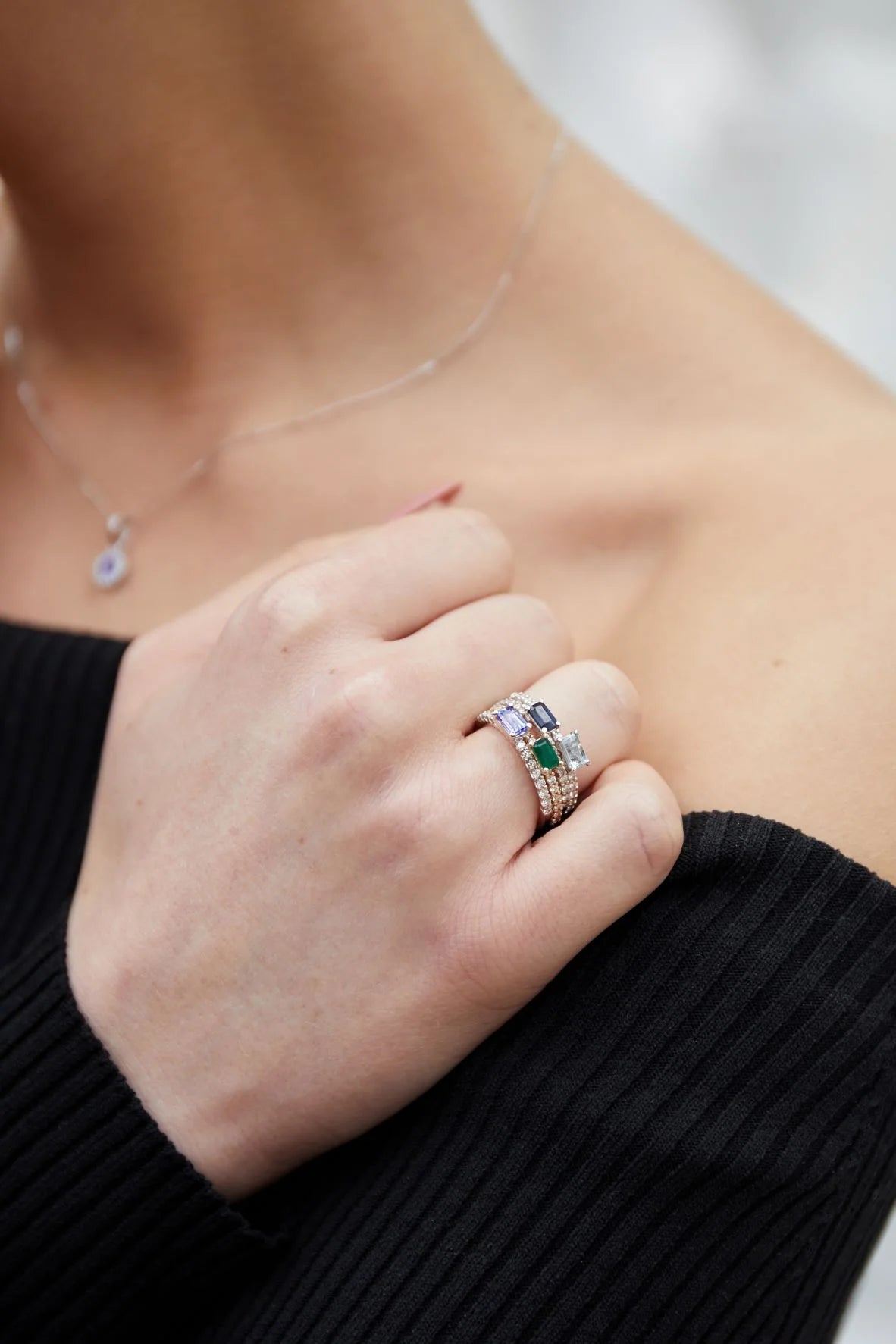Close-up of a hand wearing multiple rings with gemstones, against a blurred background.