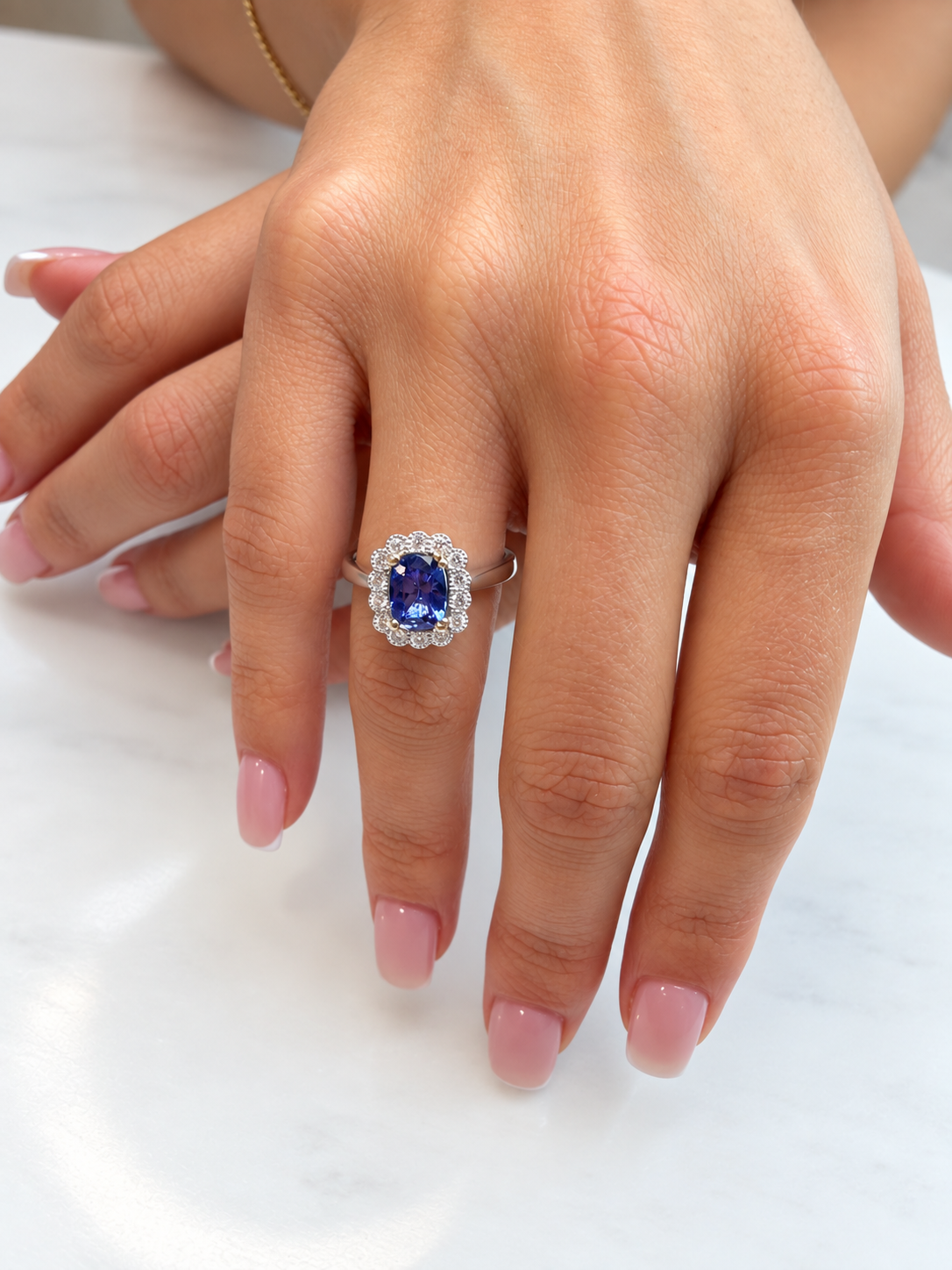 Model wearing an 18ct white gold tanzanite and diamond halo ring, showing the oval blue tanzanite and diamond surround on the hand.
