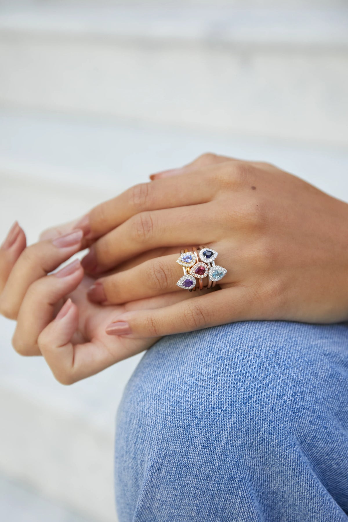 Model wearing a selection of pear-shaped birthstone and diamond cluster rings in mixed gold tones